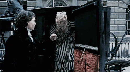 A Man And Woman Are Standing Next To Each Other In A Carriage . GIF