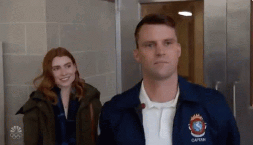 A Man And Woman Are Standing Next To Each Other In A Hallway . GIF