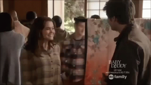 A Man And Woman Are Standing Next To Each Other In Front Of A Painting Titled Baby Daddy GIF