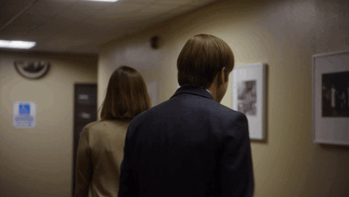 A Man And Woman Are Walking Down A Hallway With A Handicap Sign On The Wall Behind Them GIF