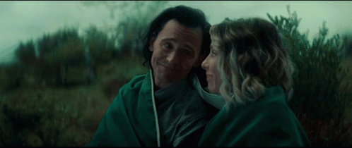 A Man And Woman Are Wrapped In A Green Blanket And Looking At Each Other GIF