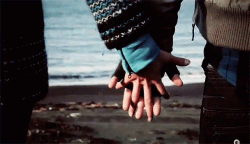 A Man And Woman Holding Hands On The Beach GIF