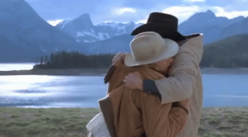 A Man And Woman Hugging In Front Of A Lake GIF