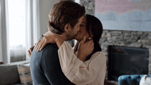 A Man And Woman Kiss In Front Of A Fireplace GIF
