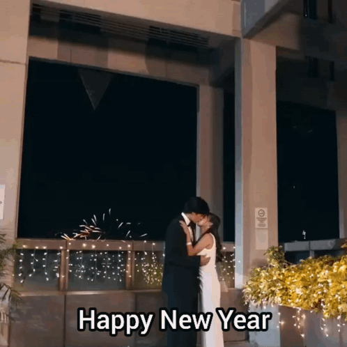 A Man And Woman Kissing In Front Of A Building With The Words Happy New Year Above Them GIF