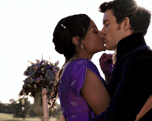 A Man And Woman Kissing In Front Of Flowers GIF