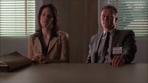 A Man And Woman Sit At A Table With A Visitor Tag GIF