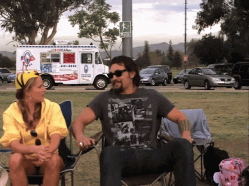 A Man And Woman Sit In Front Of An Ice Cream Truck That Says Ice Cream GIF