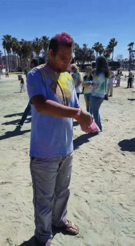 A Man Covered In Colored Powder Stands On A Sandy Beach GIF