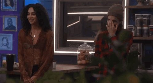 a man covering his face while standing next to a woman in a plaid shirt