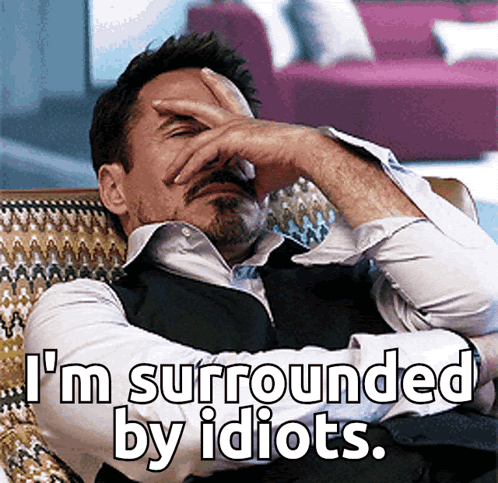 A Man Covering His Face With His Hand And The Words " I 'M Surrounded By Idiots " GIF
