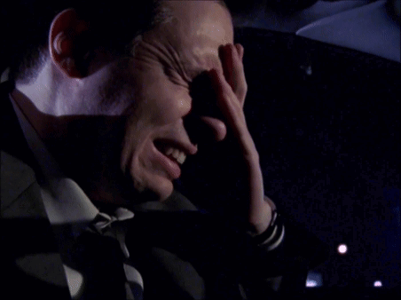 A Man Covering His Face With His Hand In A Dark Room GIF