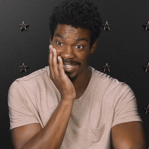A Man Covering His Face With His Hand In Front Of A Black Background With Stars GIF