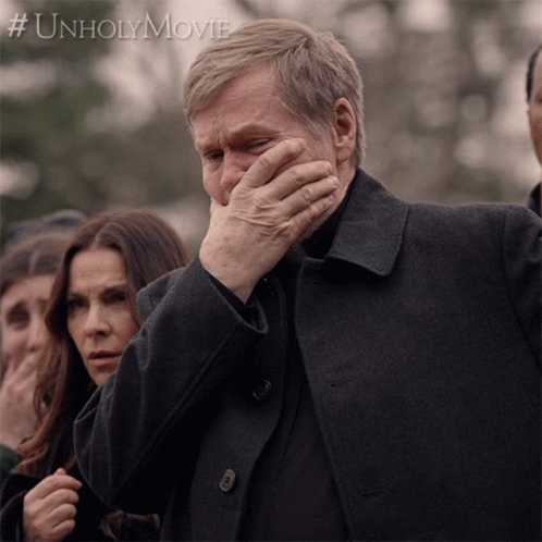 A Man Covering His Face With His Hand In Front Of A Sign That Says Unholymovie GIF