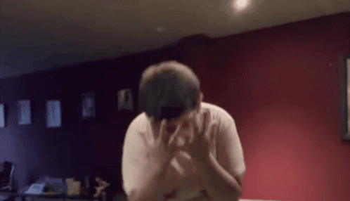 a man covering his face with his hands in a room with red walls