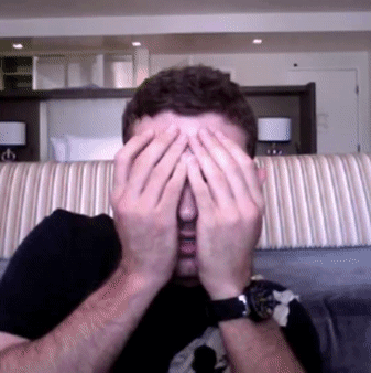 A Man Covering His Face With His Hands In Front Of A Couch GIF