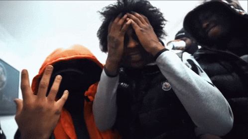 A Man Covering His Face With His Hands While Wearing An Orange Jacket GIF