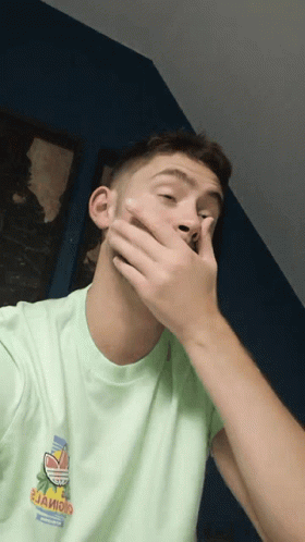 A Man Covering His Mouth With His Hand And Wearing A Green Shirt That Says " Jaioio " GIF