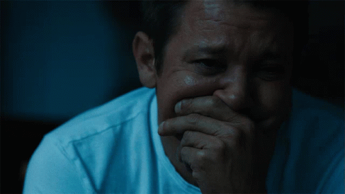 A Man Covering His Mouth With His Hand In A Dark Room GIF