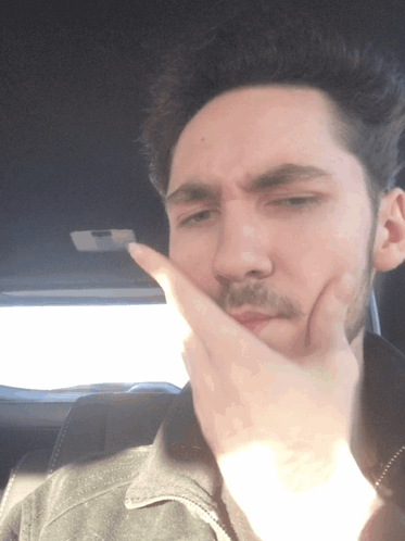 A Man Covering His Mouth With His Hand While Wearing A Black Jacket GIF