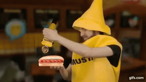 A Man Dressed As A Banana Is Holding A Hot Dog And Mustard . GIF