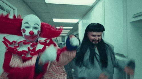 A Man Dressed As A Clown And Another Man Dressed As A Prisoner Are Dancing In A Hallway GIF