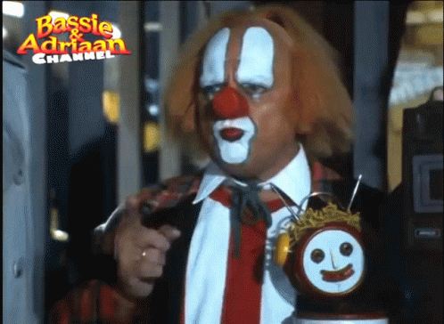 A Man Dressed As A Clown Is Holding A Clock With A Face On It And The Words Basisie & Adrian Channel Above Him GIF