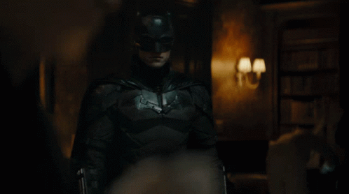 A Man Dressed As Batman Stands In A Dark Room GIF