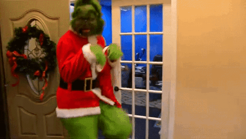 A Man Dressed As Grinch Is Standing In A Doorway . GIF