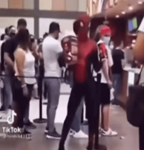 A Man Dressed As Spider Man Is Standing In Front Of A Crowd Of People . GIF