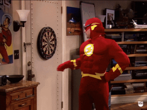 A Man Dressed As The Flash Stands In Front Of A Dart Board GIF