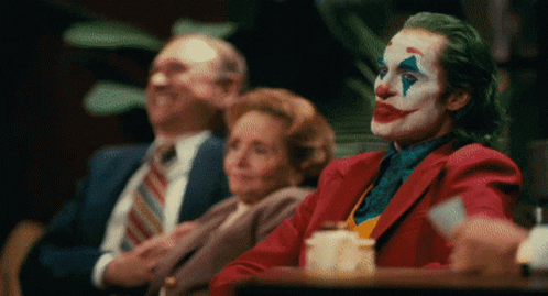 A Man Dressed As The Joker Is Sitting At A Table GIF