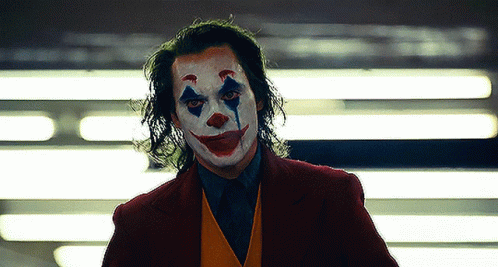 A Man Dressed As The Joker With A Clown Face Painted On His Face . GIF