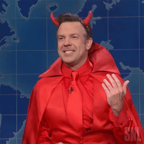 A Man Dressed In A Devil Costume With Horns And A Cape Is Waving GIF