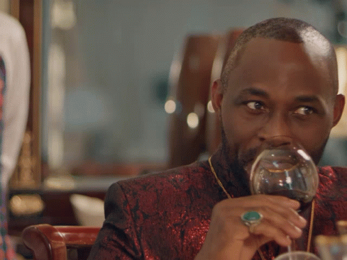 A Man Drinking A Glass Of Wine With The Words Plots Silently Below Him GIF