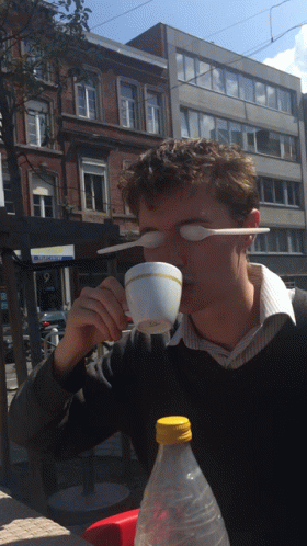 A Man Drinking From A Cup With A Plastic Spoon In His Eye GIF
