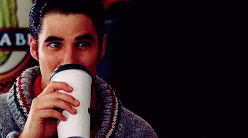 A Man Drinking From A Cup With A Sign Behind Him That Says A Be GIF