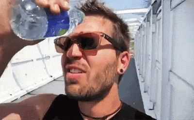 a man drinking water from a bottle while wearing sunglasses .