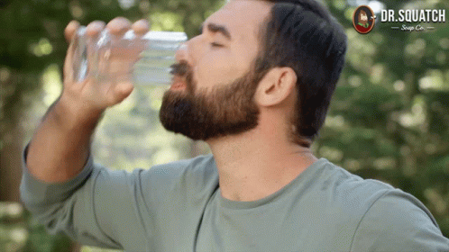 A Man Drinking Water From A Glass With A Dr. Squatch Logo On The Bottom GIF