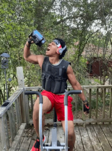 A Man Drinking Water While Riding An Exercise Bike On A Deck GIF