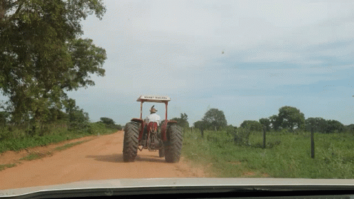 A Man Driving A Tractor On A Dirt Road With A Roof That Says ' New Holland ' On It GIF