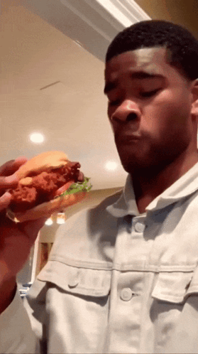 A Man Eating A Fried Chicken Sandwich With Lettuce GIF