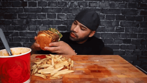 A Man Eating A Hamburger And French Fries Next To A Red Cup That Says Wendy 'S GIF