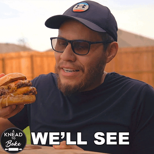 A Man Eating A Hamburger With The Words " We 'Ll See " Above Him GIF