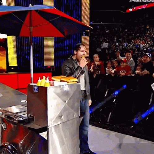 A Man Eating A Hot Dog In Front Of A Crowd That Says The Next Thing GIF