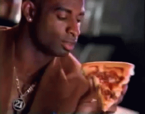 A Man Eating A Slice Of Pizza With The Number 21 On His Necklace GIF