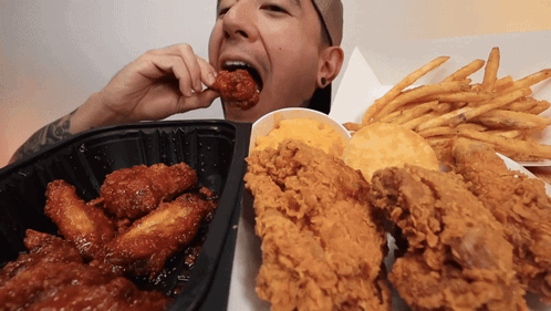 A Man Eating Fried Chicken And French Fries GIF