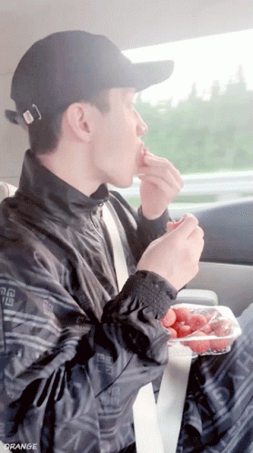 A Man Eating Strawberries In A Car With The Word Orange On The Bottom Right GIF
