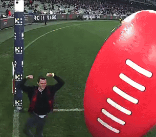 A Man Flexes His Muscles In Front Of A Giant Football GIF