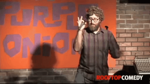 A Man Giving A Speech In Front Of A Sign That Says Rooftop Comedy GIF